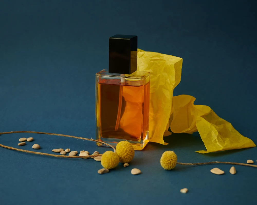 Original stock photo of an amber perfume bottle with a black cap on a blue background beside yellow paper