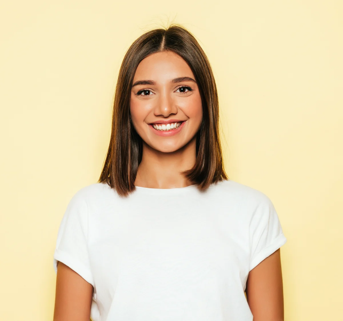 Source portrait of a smiling woman with shoulder-length brown hair and a white T-shirt against a pale yellow background