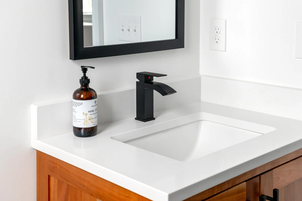 Source photo of a black waterfall tap and white inset basin beside a black-framed bathroom mirror