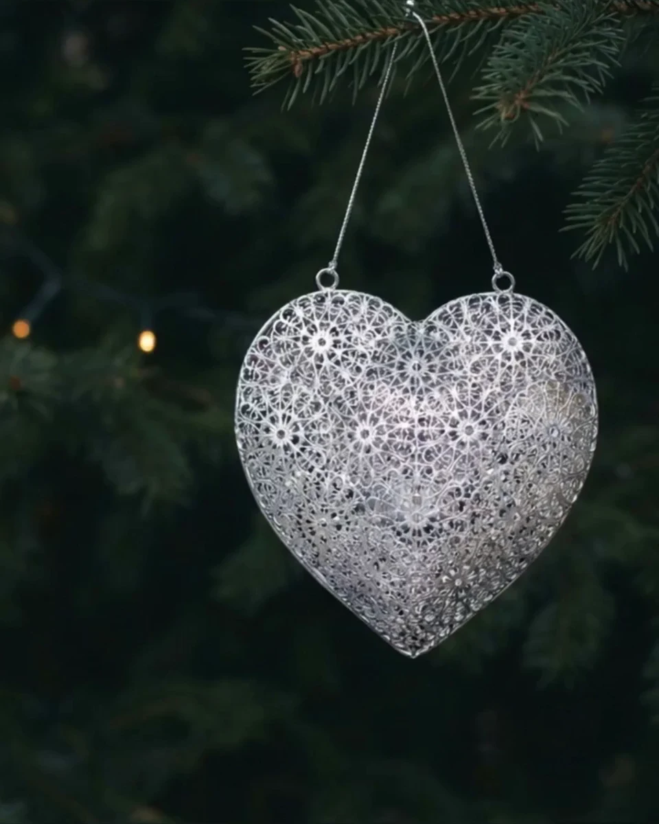 Silver filigree heart ornament hanging among evergreen branches and holiday lights